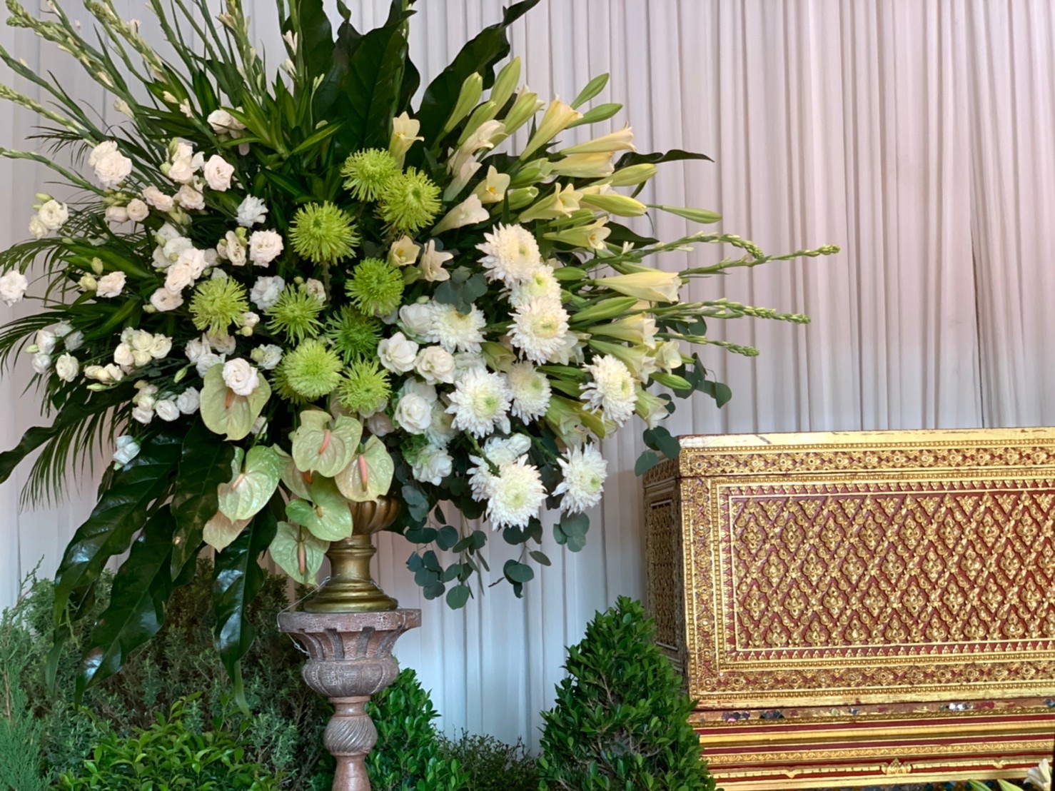 White and green floral arrangement beside gold lacquer casket